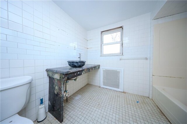 bathroom with toilet, a tub to relax in, tile walls, tile patterned floors, and sink