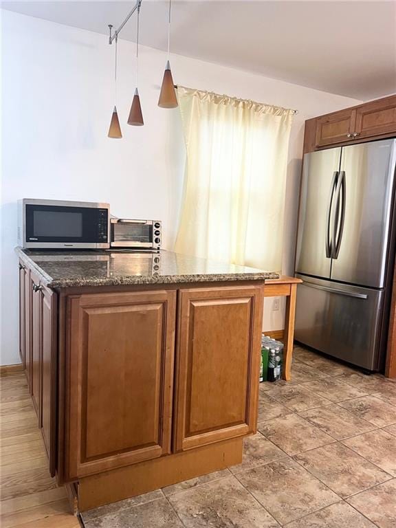 kitchen with kitchen peninsula, appliances with stainless steel finishes, hanging light fixtures, and dark stone counters