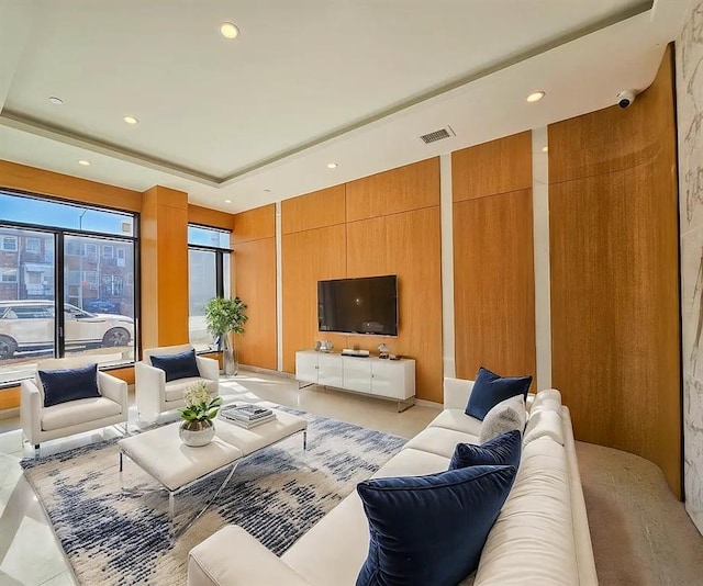 living area featuring a tray ceiling, visible vents, wood walls, and recessed lighting