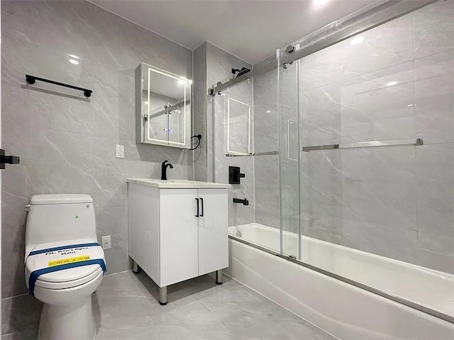 full bathroom featuring toilet, vanity, shower / bath combination with glass door, and tile walls