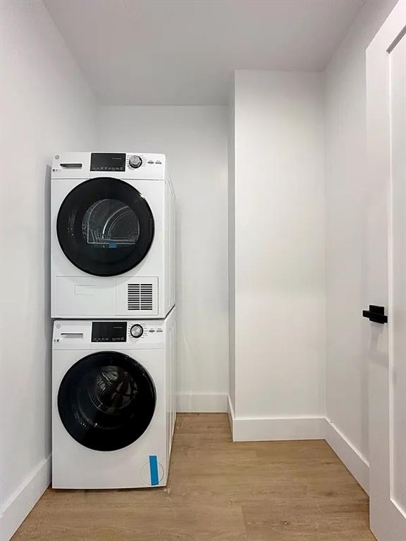 laundry room featuring stacked washing maching and dryer and light hardwood / wood-style floors