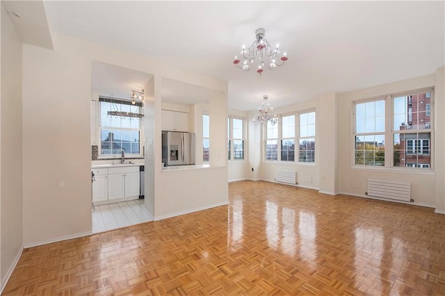 unfurnished living room with an inviting chandelier, baseboards, and a sink