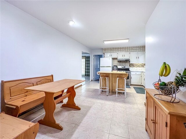 kitchen with a kitchen bar, a kitchen island, white fridge, stainless steel range oven, and white cabinetry