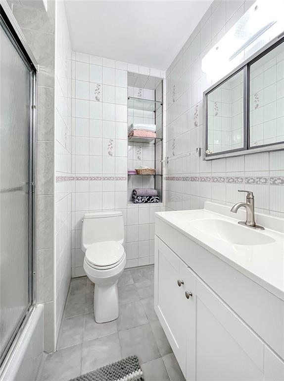 full bathroom featuring vanity, shower / bath combination with glass door, tile patterned floors, toilet, and tile walls