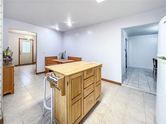 kitchen with an inviting chandelier, a kitchen island, fridge, a breakfast bar area, and light tile patterned flooring