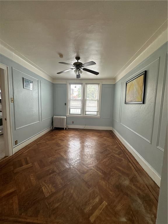 empty room with ceiling fan, ornamental molding, radiator, and dark parquet floors