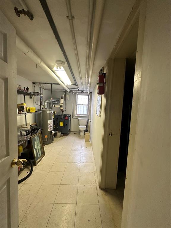 basement featuring water heater and light tile patterned flooring