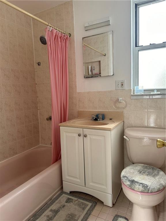 full bathroom featuring a wealth of natural light, tile walls, vanity, and shower / bath combo with shower curtain