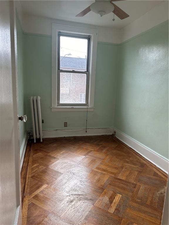 unfurnished room featuring radiator heating unit, ceiling fan, and parquet floors