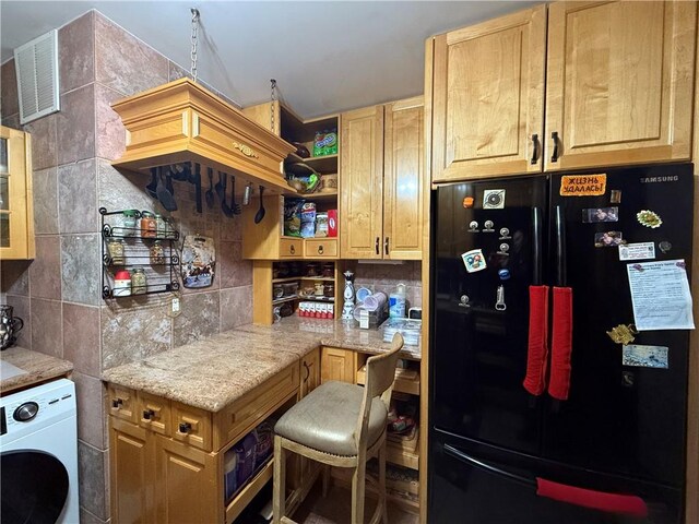 kitchen featuring a breakfast bar, black fridge, light stone counters, washer / clothes dryer, and backsplash