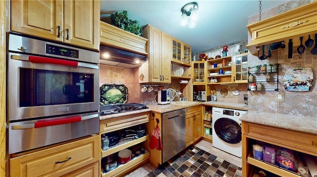 kitchen with appliances with stainless steel finishes, washer / clothes dryer, sink, decorative backsplash, and light stone countertops