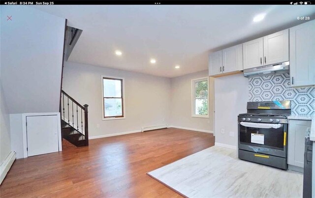 kitchen featuring stainless steel gas range oven, backsplash, a baseboard heating unit, white cabinets, and light hardwood / wood-style flooring