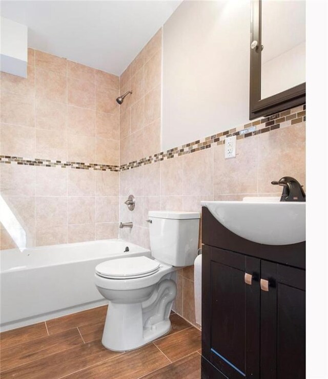 full bathroom featuring toilet, vanity, tiled shower / bath combo, and tile walls