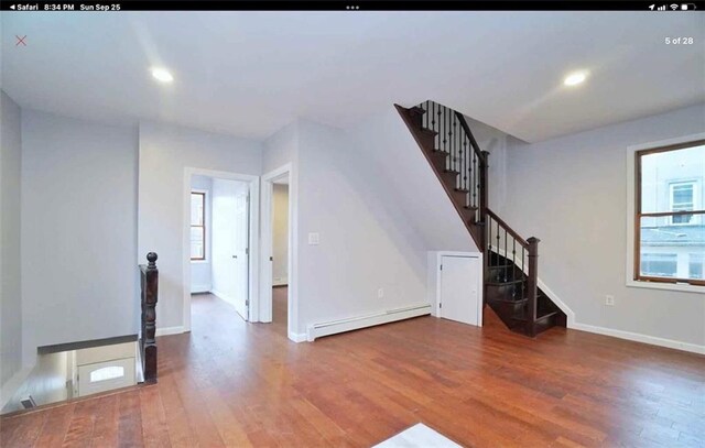 unfurnished living room with wood-type flooring and a baseboard heating unit