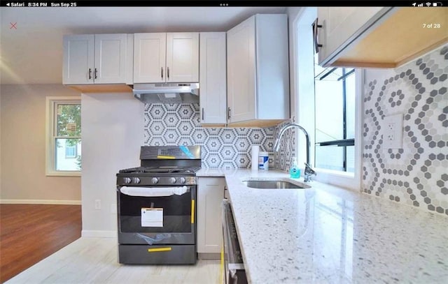 kitchen featuring light stone counters, sink, black gas range, light hardwood / wood-style floors, and white cabinetry