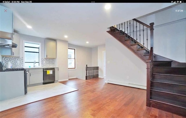 kitchen featuring decorative backsplash, stainless steel appliances, a healthy amount of sunlight, a baseboard radiator, and hardwood / wood-style floors