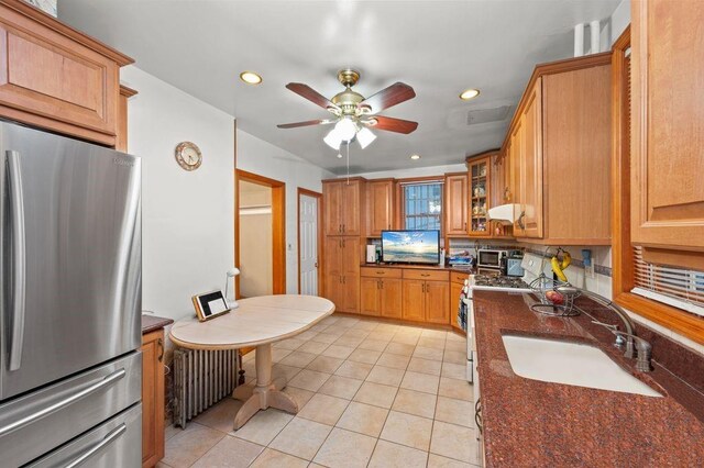 kitchen featuring radiator heating unit, stainless steel refrigerator, sink, dark stone countertops, and gas range oven