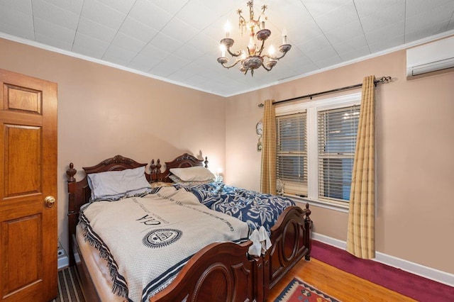 bedroom with baseboards, wood finished floors, crown molding, an AC wall unit, and a notable chandelier