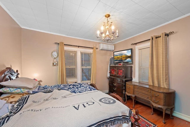 bedroom with a wall unit AC, wood finished floors, baseboards, ornamental molding, and an inviting chandelier