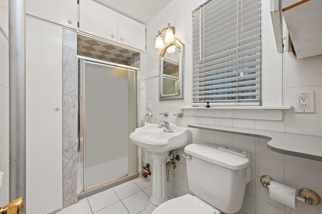 bathroom with tile patterned flooring, toilet, tile walls, and a shower with shower door