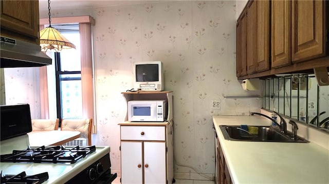 kitchen featuring hanging light fixtures, sink, black gas range, and ventilation hood