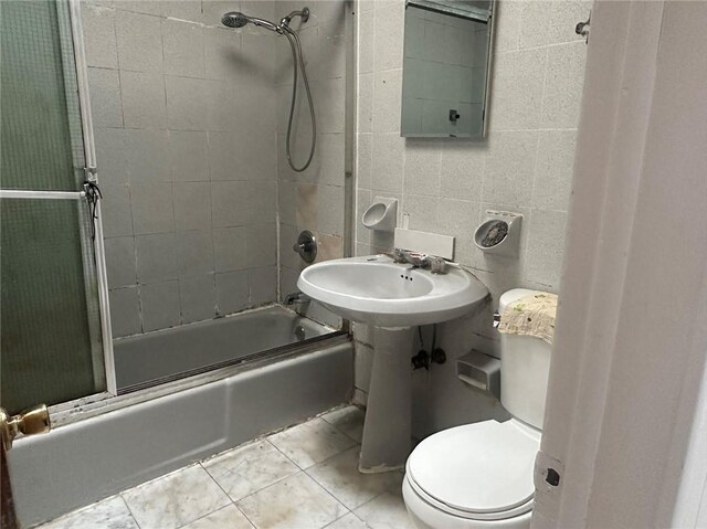 bathroom featuring tile patterned flooring, enclosed tub / shower combo, tile walls, and toilet