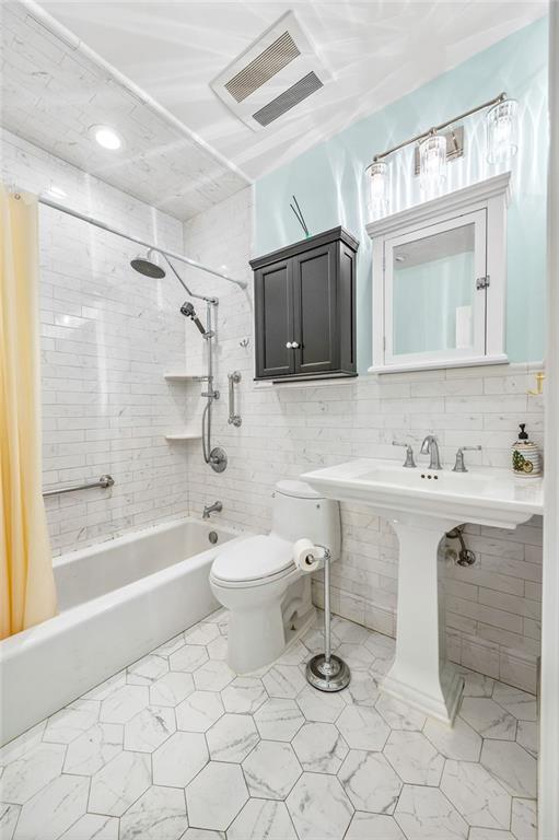 bathroom with tile walls, toilet, shower / bathtub combination with curtain, and tasteful backsplash