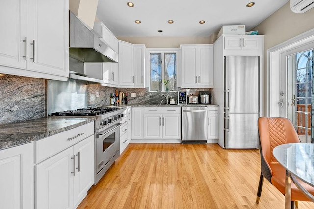 kitchen featuring ventilation hood, a wall mounted AC, high end appliances, and white cabinetry