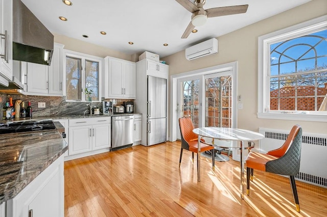 kitchen featuring extractor fan, stainless steel appliances, dark stone counters, white cabinets, and an AC wall unit