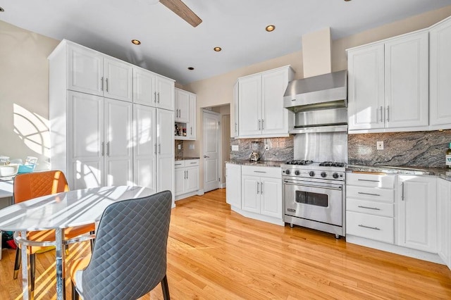 kitchen with white cabinetry, wall chimney exhaust hood, premium range, and tasteful backsplash