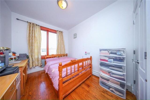 bedroom with vaulted ceiling, dark hardwood / wood-style flooring, and a baseboard heating unit