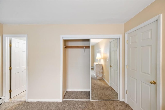 unfurnished bedroom with a closet, baseboards, baseboard heating, and carpet flooring