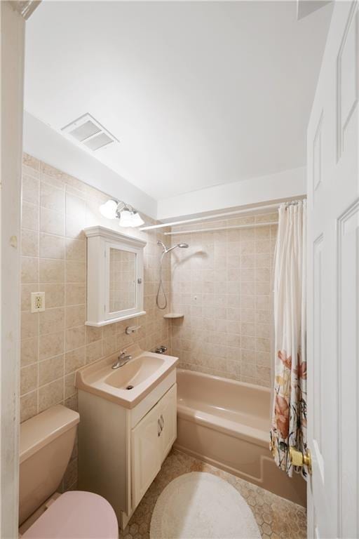 full bathroom featuring shower / tub combo, visible vents, toilet, vanity, and tile walls