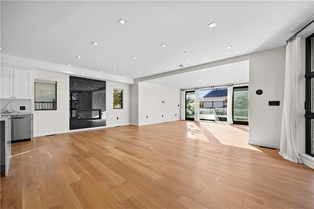 unfurnished living room featuring baseboards, light wood finished floors, a premium fireplace, and recessed lighting