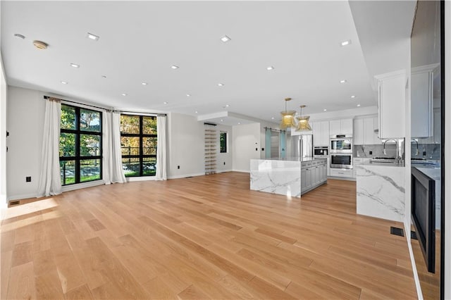 unfurnished living room featuring visible vents, a sink, light wood-style flooring, and recessed lighting