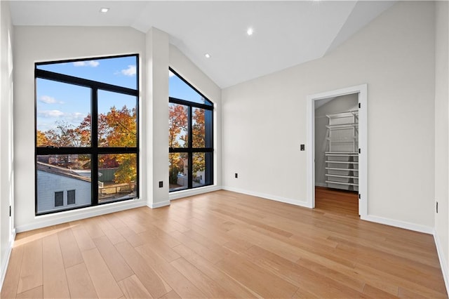 unfurnished room featuring vaulted ceiling, light wood-style flooring, and a healthy amount of sunlight