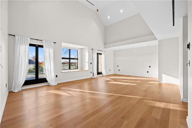 unfurnished living room featuring high vaulted ceiling, light wood-type flooring, baseboards, and recessed lighting