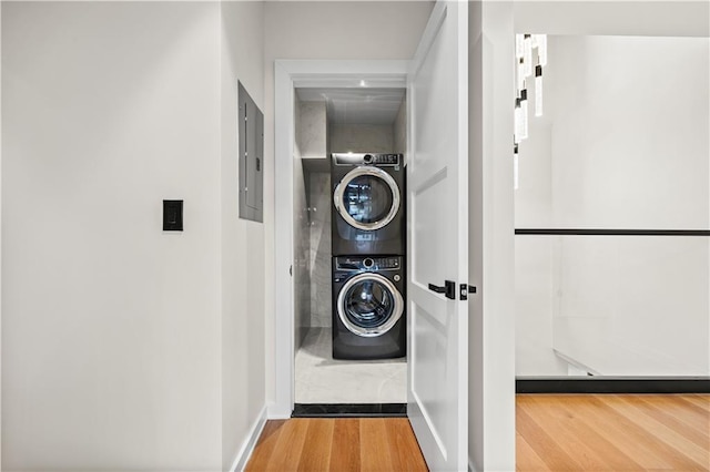 clothes washing area with laundry area, stacked washer / dryer, wood finished floors, baseboards, and electric panel