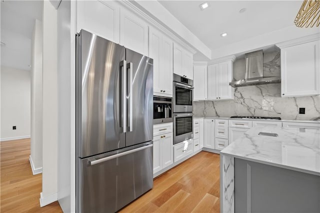 kitchen with stainless steel appliances, wall chimney range hood, backsplash, and white cabinets