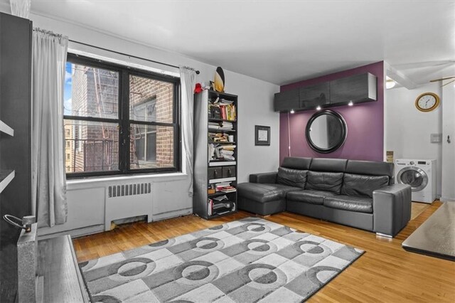 living room with washer / clothes dryer, ceiling fan, light hardwood / wood-style flooring, and radiator heating unit