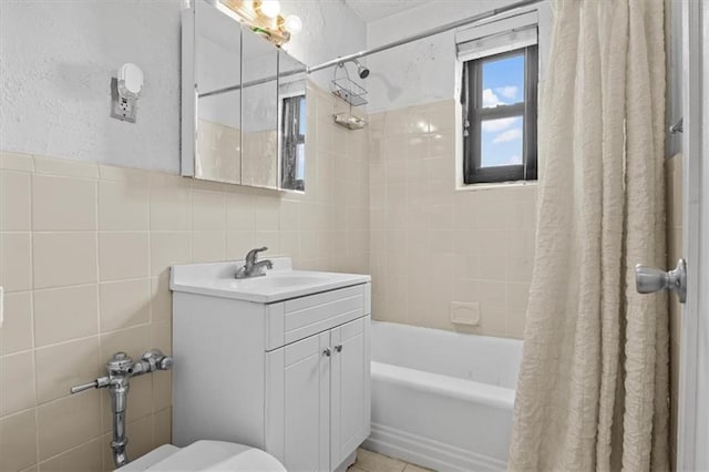 full bathroom featuring shower / tub combo, a textured wall, toilet, vanity, and tile walls