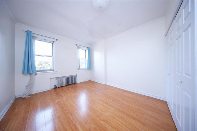 empty room featuring crown molding, radiator heating unit, and light hardwood / wood-style flooring