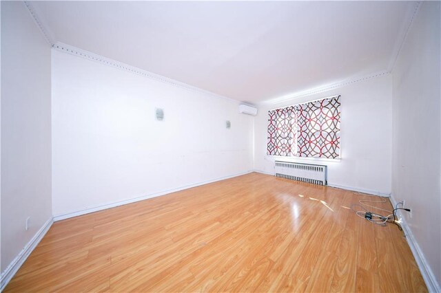 unfurnished living room with hardwood / wood-style flooring, crown molding, an AC wall unit, and radiator