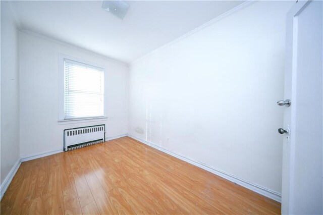 spare room with ornamental molding, radiator heating unit, and light wood-type flooring