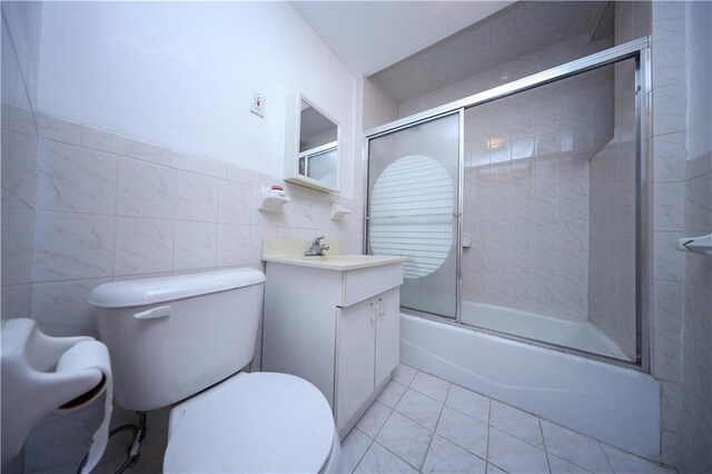 full bathroom featuring tile walls, tile patterned flooring, bath / shower combo with glass door, vanity, and toilet