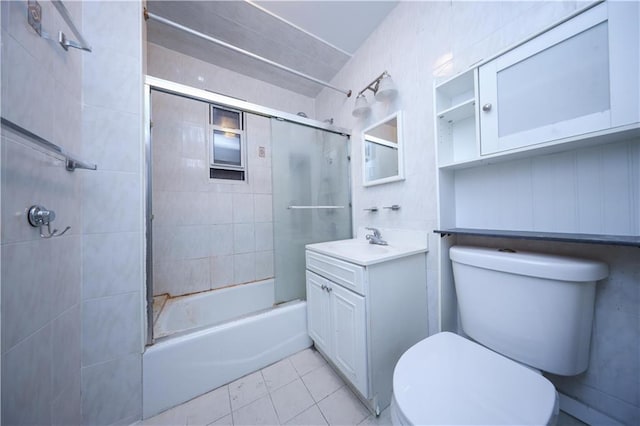 full bathroom featuring combined bath / shower with glass door, tile walls, vanity, tile patterned floors, and toilet