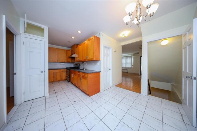 kitchen featuring tasteful backsplash, a notable chandelier, black range with gas stovetop, and sink