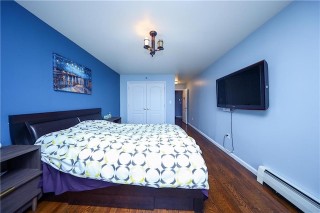 bedroom with a baseboard heating unit, dark wood-style flooring, a closet, and baseboards