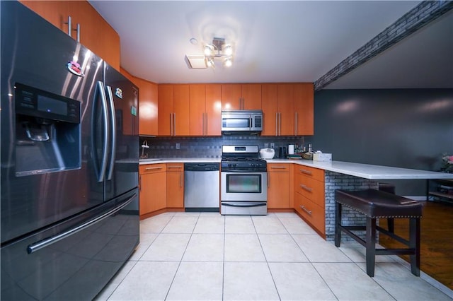 kitchen featuring light countertops, decorative backsplash, appliances with stainless steel finishes, light tile patterned flooring, and a peninsula