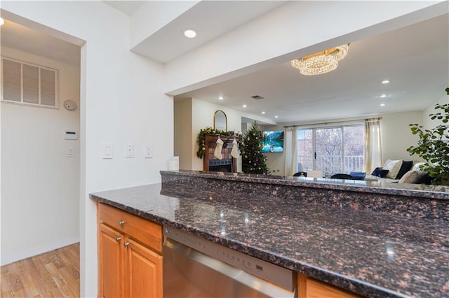 kitchen with light wood-type flooring, a chandelier, dishwasher, and dark stone counters